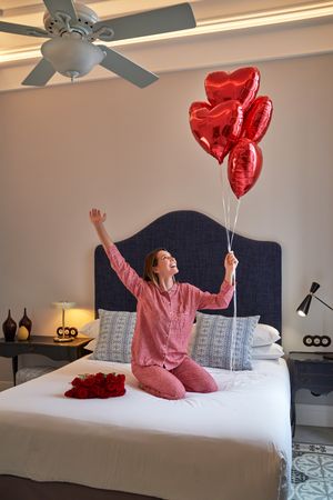 Excited woman on bed with bunch of red heart balloons