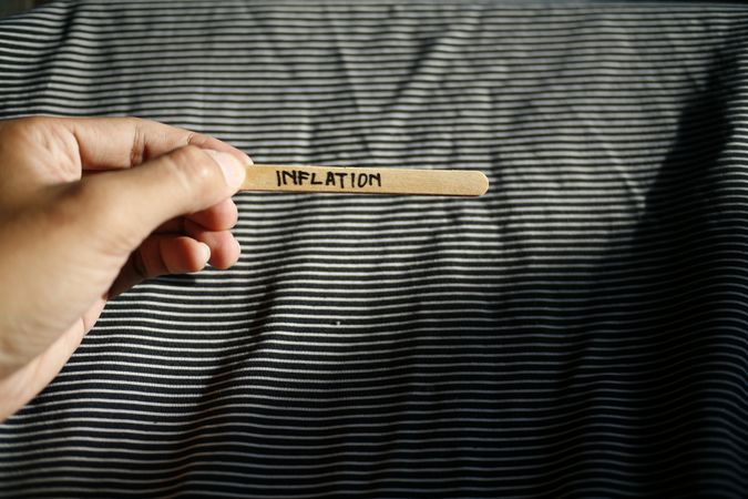 The word “inflation” written on wooden stick being held by person
