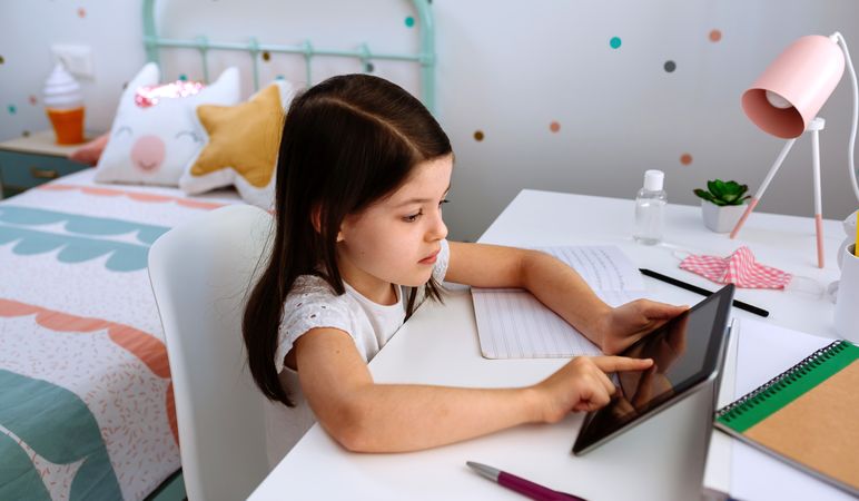 Girl studying at home with tablet and mask on table