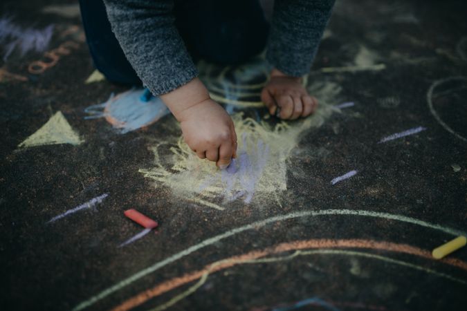 Child scribbling with chalk on the pavement