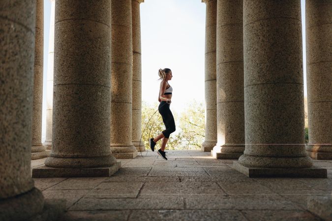 Woman in fitness wear doing skipping standing near stone pillars