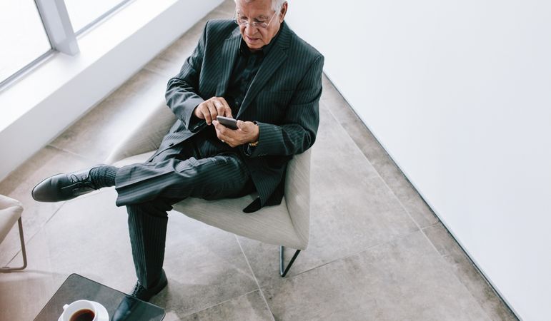 Man in business suit sitting in office lobby using cell phone in office lobby