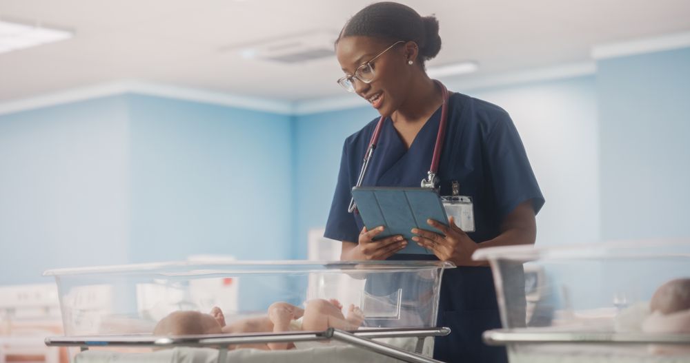 Nurse Using Tablet Computer Checking Up on a Newborn Baby in Maternity Ward Facility.