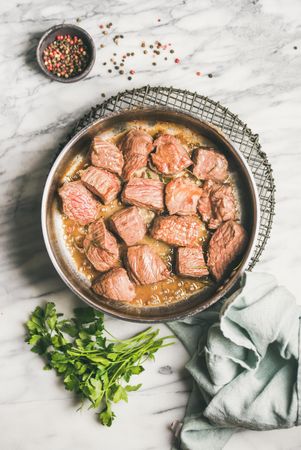 Chunks of braised beef in pan, with parsley and peppercorn