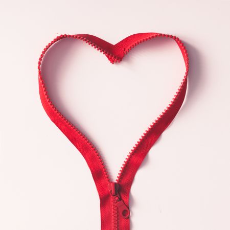Red zipper in shape of a heart on light background