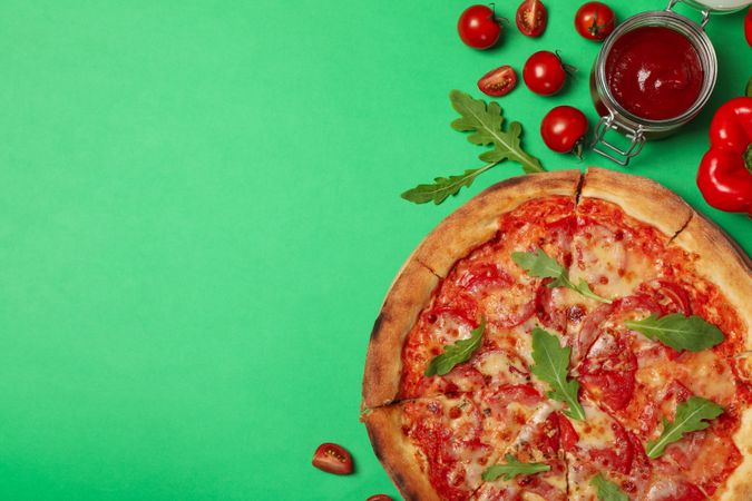 Tasty pizza and ingredients on green background