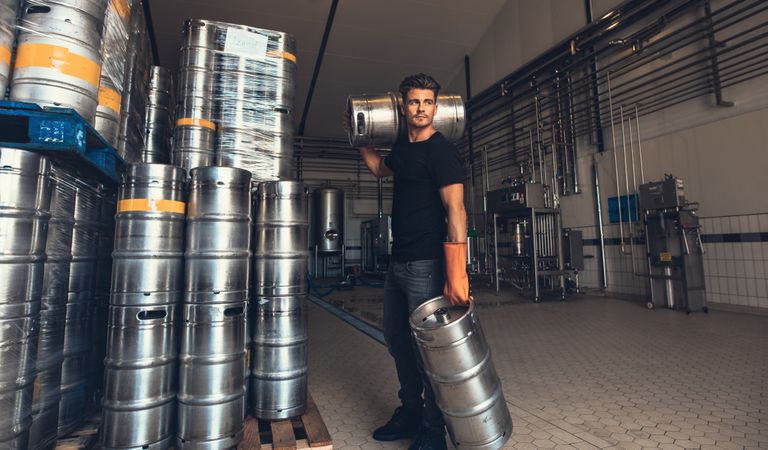 Young male brewer carrying kegs at brewery factory