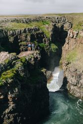 Two men on edge of cliff over waterfall, portrait