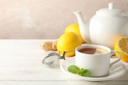 Cup of tea with lemon, mint, strainer, ginger and teapot on wooden background, copy space