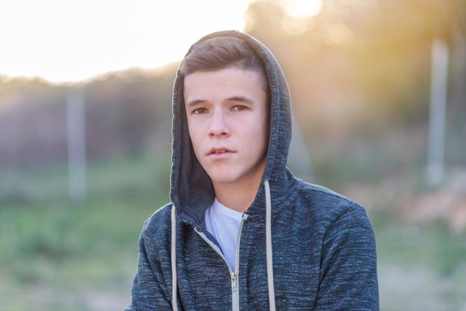 Teenage male in hoodie standing in field looking at camera