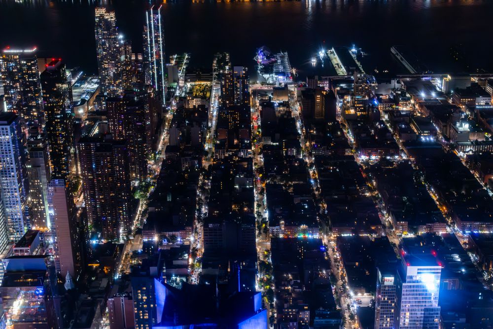 Top Down Aerial View of New York City Streets at Night with Visible Grid System, Business and Residential Building Roofs. Busy Center with Traffic, Cars, Yellow Taxis, Commercial Vehicles, Pedestrians