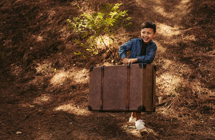 Boy on a park path with old suitcase in hands