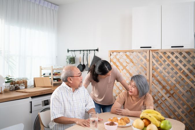 Asian family with mature parents and adult daughter enjoying breakfast at home