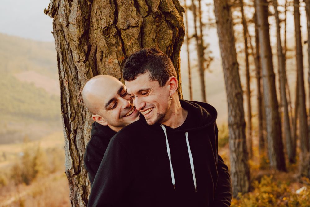 Smiling men hugging near tree in forest on hill