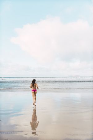 Woman in swimwear running near sea