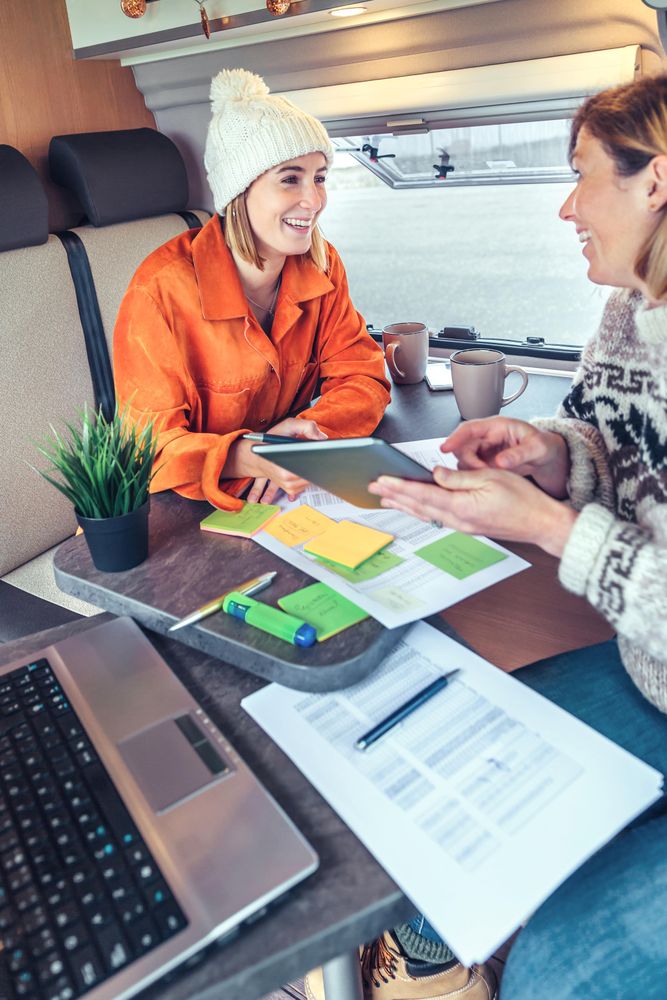 Two females working remotely in back of van while on a road trip, vertical