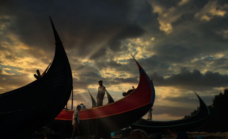 Two men beside boats on seashore during sunset