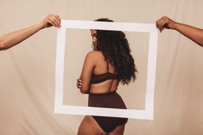 Body positive woman standing behind a picture frame in brown underwear