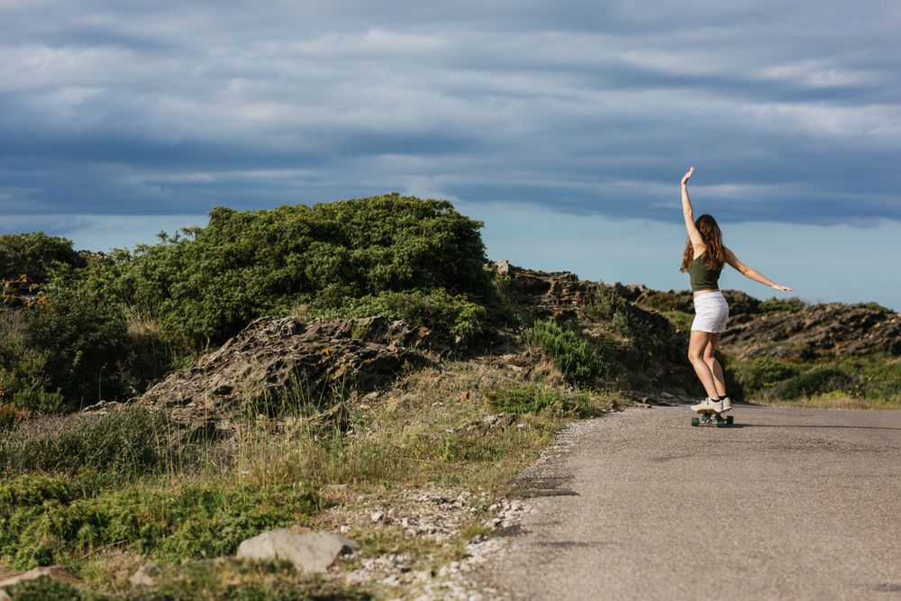 Anonymous woman riding longboard on asphalt road