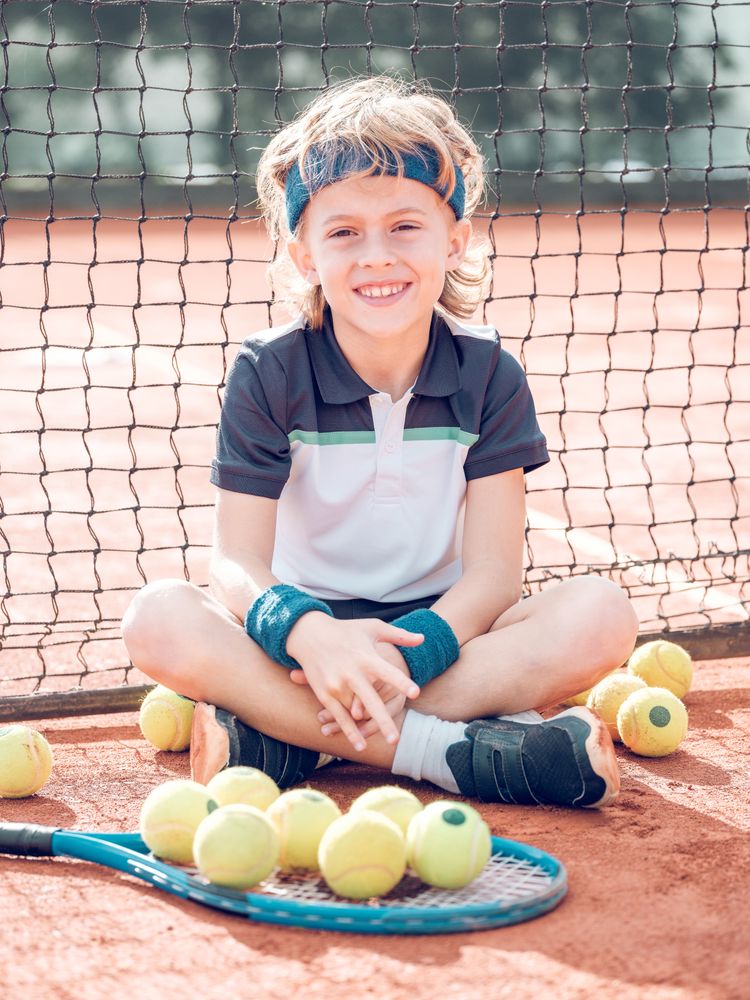 Content kid tennis player resting on court and smiling after mat