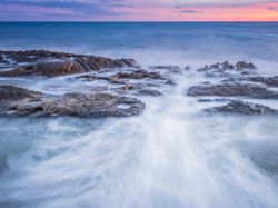 Sea waving near rough rocks during sunset