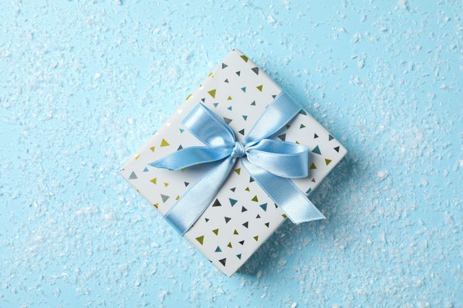 Snow and present with bow on blue background, space for text