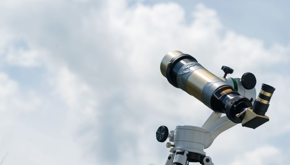 Brass telescope against cloudy sky background.