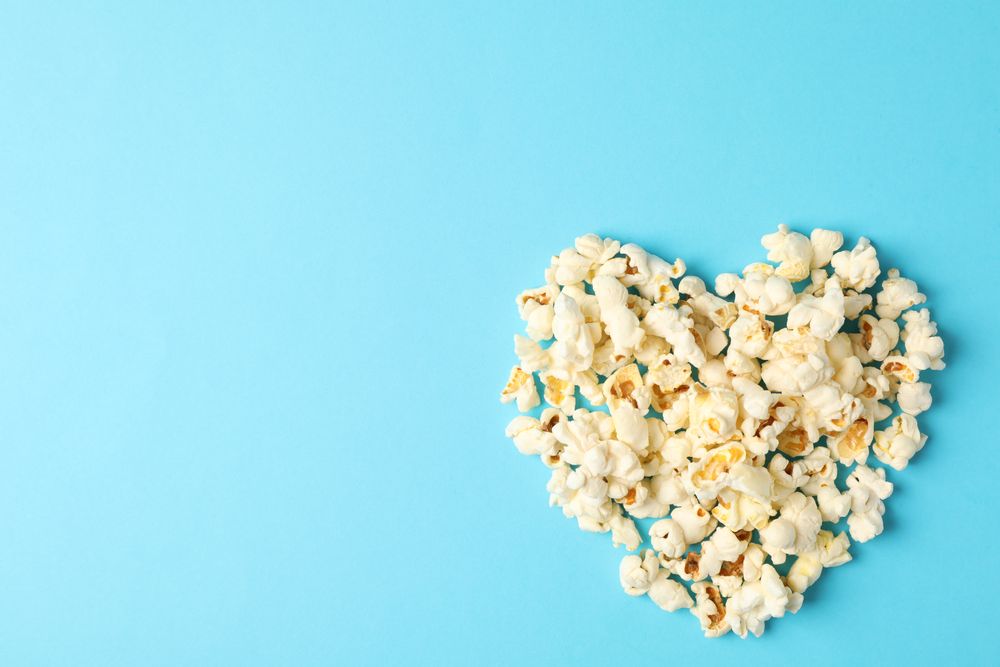 Flat lay composition with popcorn heart on blue background, space for text