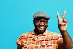 Portrait of a happy young man holding victory hand sign, isolated on blue background