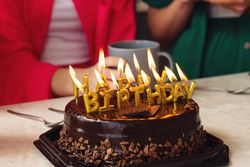 Birthday cake with golden candles burning, surrounded by chocolate pieces.