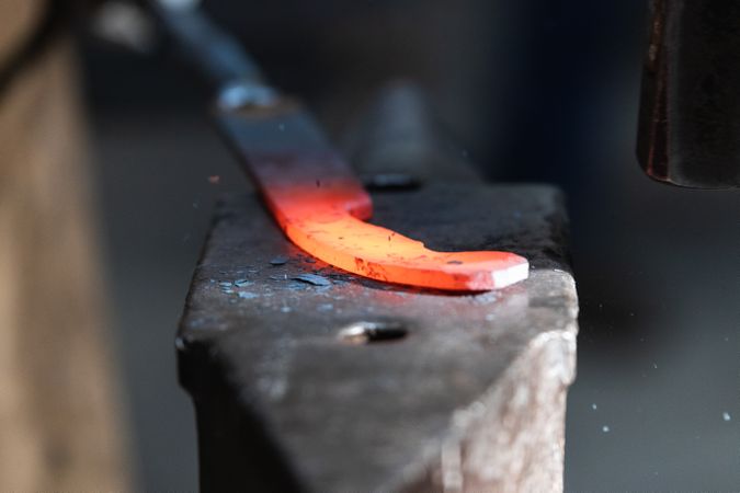 Blacksmiths forging hot metal with hammer in workshop