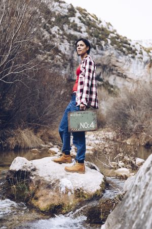 Woman with case jumping on rocks above stream