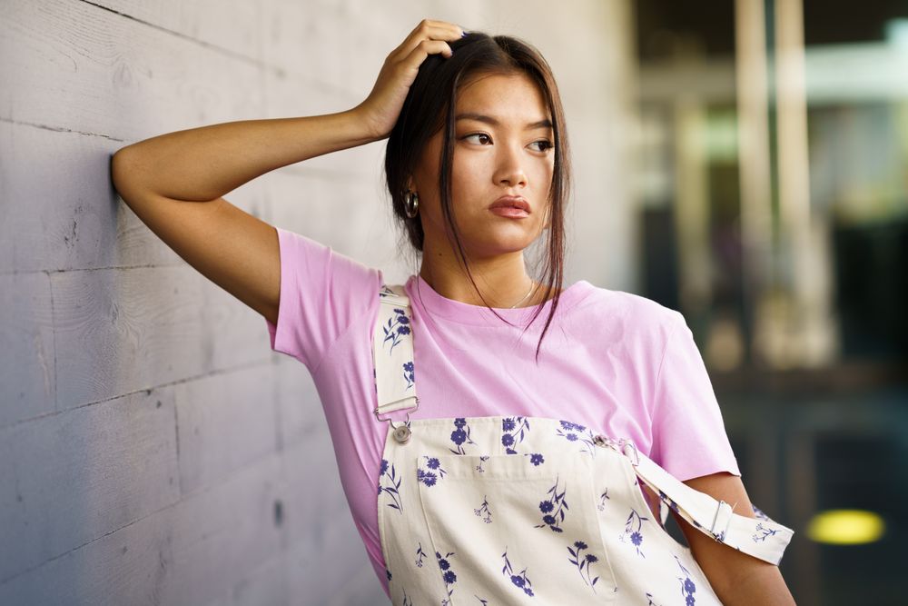 Serious female in overalls leaning elbow and resting head on wall