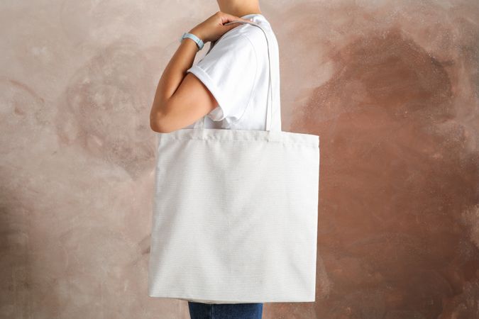 Young woman holding tote bag against brown background, empty space