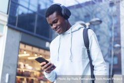 Young Black man standing in the street while listening music on headphones bYqO76