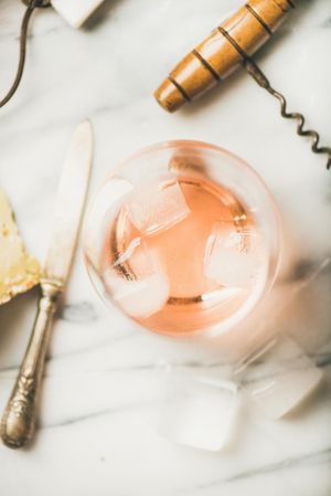 Rose wine in glass on marble table with corkscrew and cheese knife