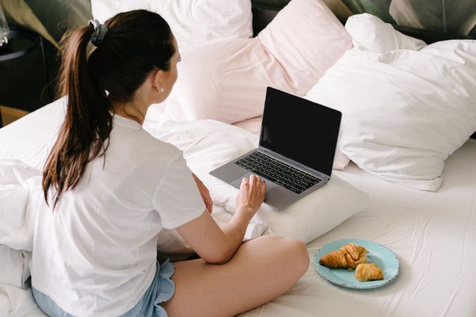 Back view of anonymous woman using laptop on bed