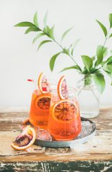 Two glasses of an orange cocktail with orange slices, and leaves in background, vertical composition