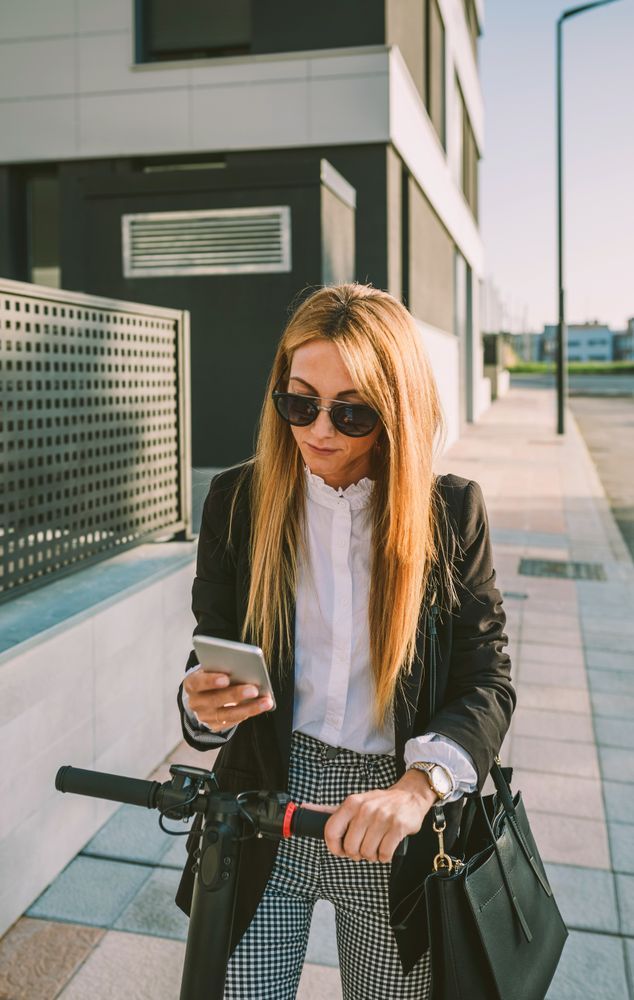 Businesswoman with e-scooter looking at cellphone