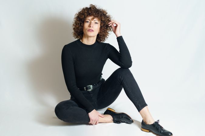 Woman in dark outfit sitting on floor with hand up to hair