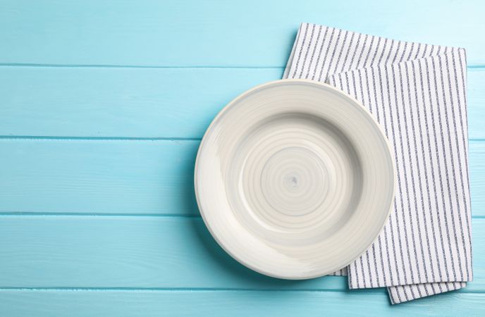 Kitchen towel with plate on wooden background, top view