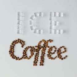 Ice cubes shaped in the word “ICE” and coffee beans spelling “Coffee” on bright background