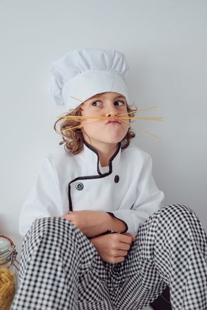Funny boy in chef uniform making face with spaghetti sticks