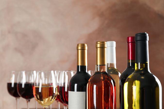 Bottles and glasses with wine against brown background, copy space
