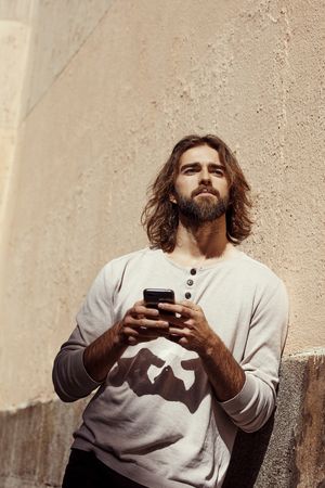 Man holding phone in hands leaning on wall