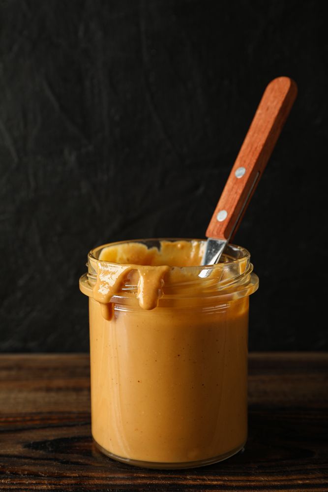 Glass jar with peanut butter and spoon on wooden table against dark background, space for text
