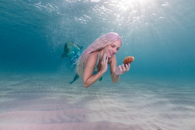 Blond fairytale female mermaid exploring underwater