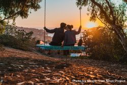 Back view of man and woman kissing and sitting on blue swing in nature 0LJmr4