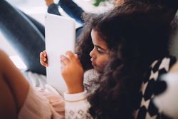 Little girl lying in bed reading a tablet
