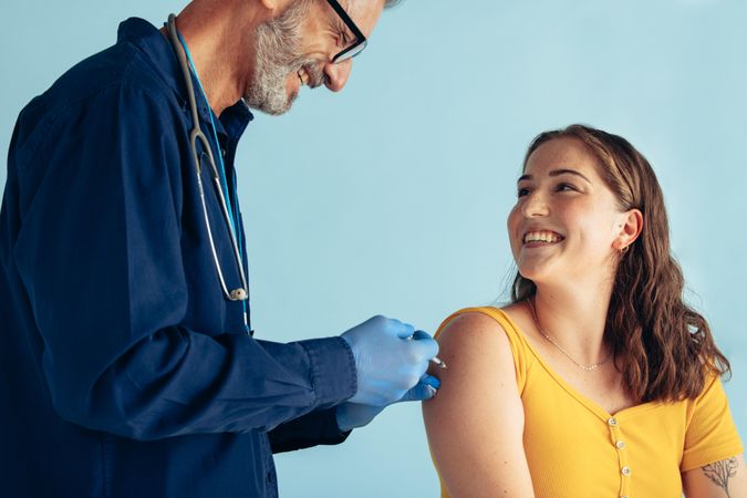 Mature doctor giving injection to woman on blue background